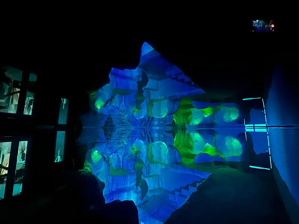 Espace du L’Ôlà dans la pénombre, éclairé de projections bleues et vertes Espace du L’Ôlà dans la pénombre, éclairé de projections bleues et vertes